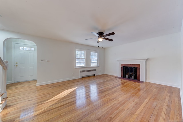 unfurnished living room with radiator heating unit, light wood-type flooring, a brick fireplace, and ceiling fan