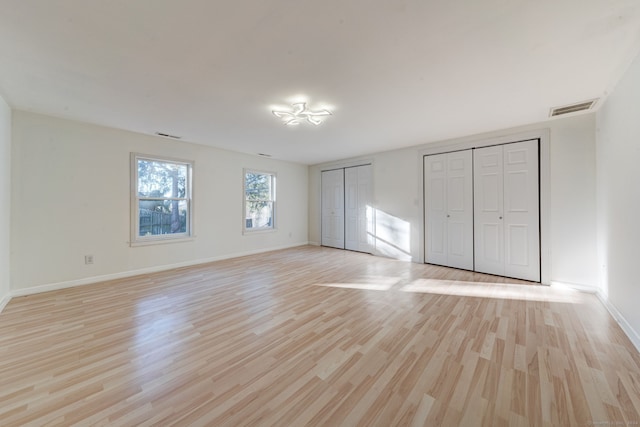 unfurnished bedroom with light wood-type flooring and two closets