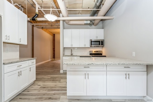 kitchen with backsplash, white cabinetry, stainless steel appliances, and light hardwood / wood-style flooring