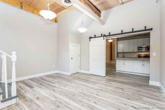 kitchen featuring stainless steel appliances, beam ceiling, a barn door, light hardwood / wood-style floors, and hanging light fixtures