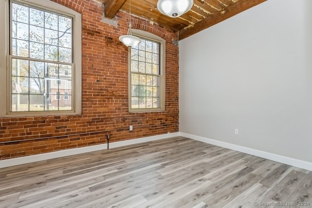 unfurnished room featuring beam ceiling, light hardwood / wood-style flooring, wooden ceiling, and brick wall