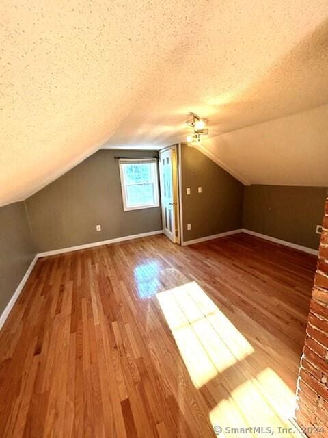 additional living space with hardwood / wood-style floors, a textured ceiling, and vaulted ceiling