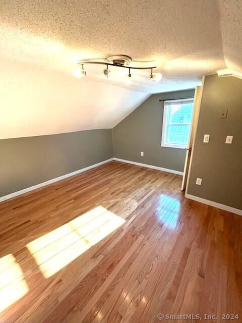 bonus room with lofted ceiling, hardwood / wood-style floors, and a textured ceiling