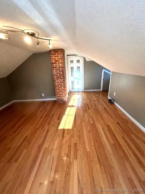 additional living space featuring vaulted ceiling, light hardwood / wood-style flooring, and a textured ceiling