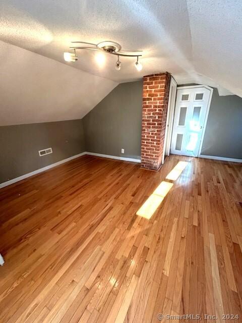 additional living space featuring a textured ceiling, light hardwood / wood-style flooring, and lofted ceiling