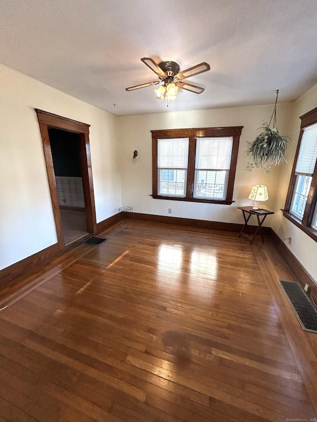 unfurnished room with a wealth of natural light, dark hardwood / wood-style flooring, ceiling fan, and a textured ceiling