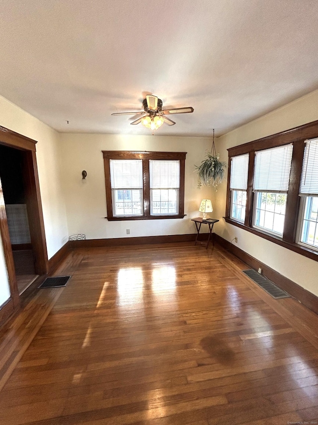 empty room with a wealth of natural light, dark hardwood / wood-style flooring, and ceiling fan