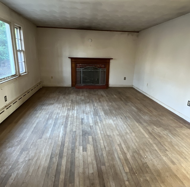 unfurnished living room with wood-type flooring, a baseboard radiator, and a brick fireplace