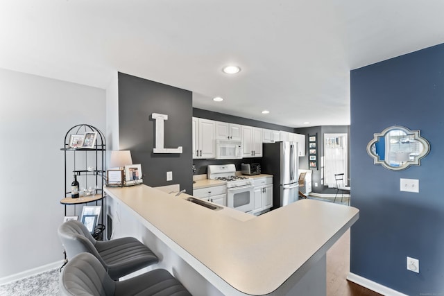 kitchen featuring white appliances, sink, kitchen peninsula, white cabinetry, and a breakfast bar area