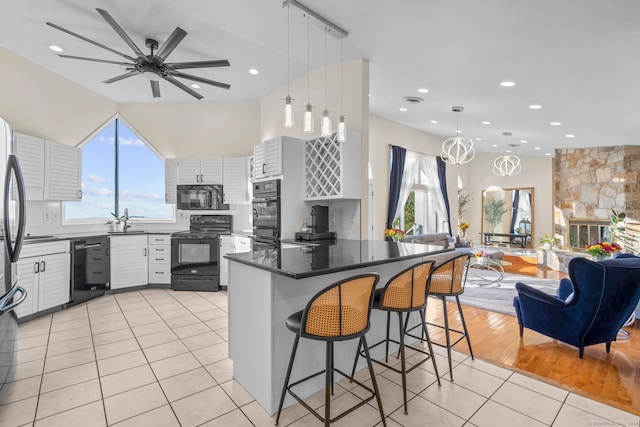 kitchen featuring plenty of natural light, black appliances, white cabinets, decorative light fixtures, and a breakfast bar area