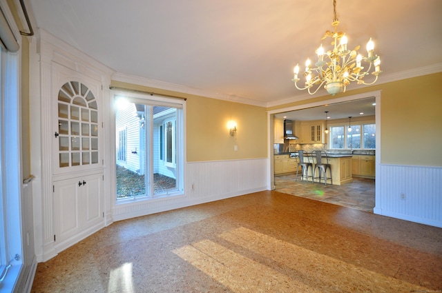 unfurnished living room featuring a notable chandelier, a wainscoted wall, and crown molding