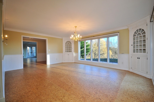 empty room with a chandelier, a decorative wall, ornamental molding, and wainscoting