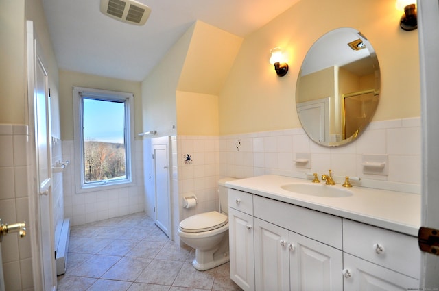 bathroom featuring tile patterned flooring, vaulted ceiling, toilet, vanity, and tile walls