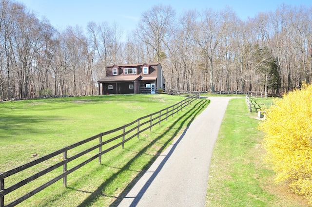 view of yard with a wooded view, fence, and driveway