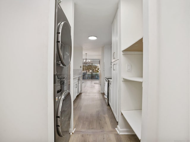 corridor with a notable chandelier, hardwood / wood-style flooring, and stacked washer and dryer