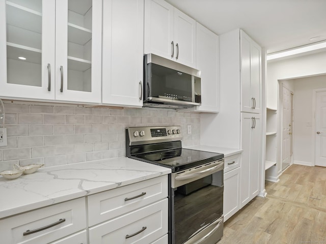 kitchen featuring white cabinets, light wood-type flooring, decorative backsplash, light stone countertops, and appliances with stainless steel finishes