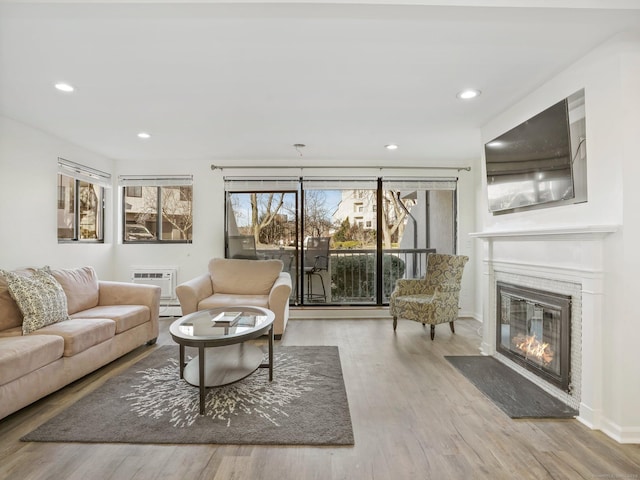 living room with an AC wall unit, a baseboard heating unit, and light hardwood / wood-style flooring