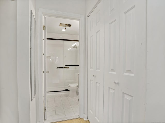 bathroom featuring toilet, a shower with door, and tile patterned floors