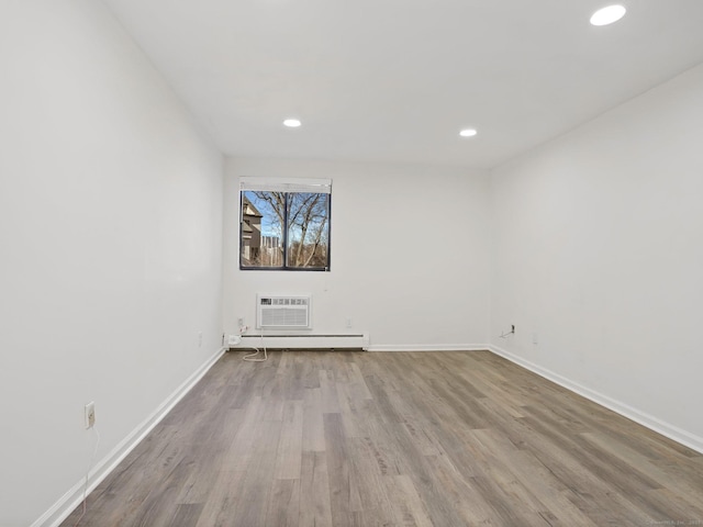 empty room with a wall unit AC, a baseboard heating unit, and light hardwood / wood-style floors