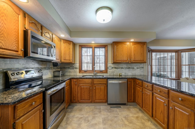 kitchen with appliances with stainless steel finishes, a textured ceiling, dark stone counters, and sink