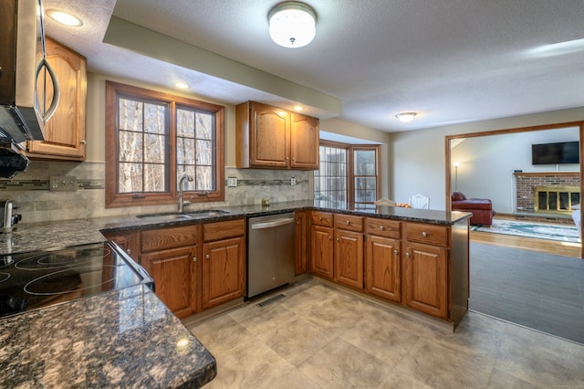 kitchen featuring kitchen peninsula, appliances with stainless steel finishes, a textured ceiling, sink, and a fireplace