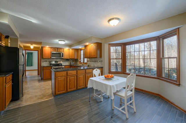 kitchen featuring appliances with stainless steel finishes, backsplash, a textured ceiling, sink, and dark stone countertops