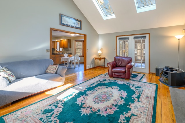 living room featuring french doors, light hardwood / wood-style flooring, high vaulted ceiling, and a skylight