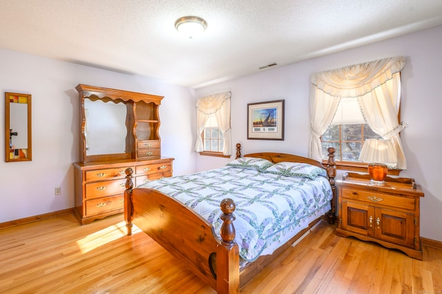 bedroom featuring a textured ceiling, light hardwood / wood-style floors, and multiple windows