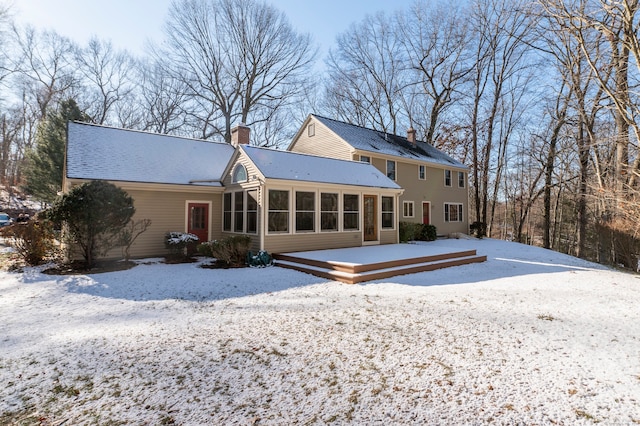 snow covered back of property featuring a sunroom and a deck