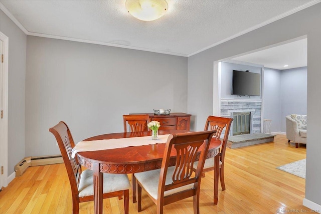 dining room featuring a baseboard heating unit, a stone fireplace, ornamental molding, a textured ceiling, and light hardwood / wood-style floors