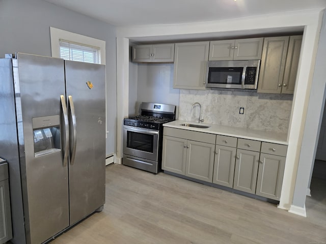 kitchen featuring sink, light hardwood / wood-style flooring, gray cabinets, decorative backsplash, and appliances with stainless steel finishes