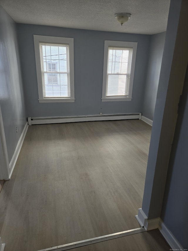 spare room featuring baseboard heating, hardwood / wood-style floors, and a textured ceiling