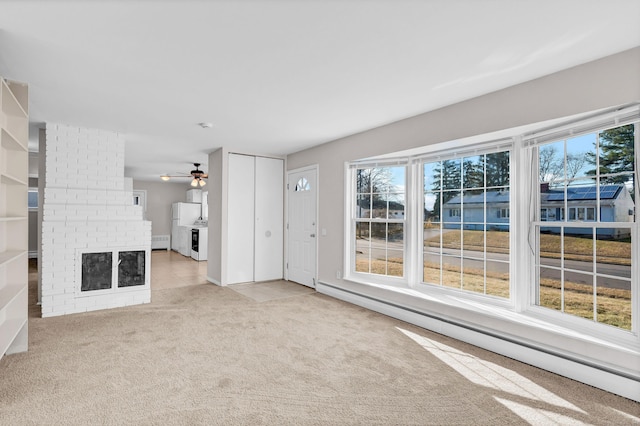 unfurnished living room featuring light carpet, baseboard heating, and a healthy amount of sunlight