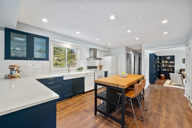 kitchen with blue cabinets, wood-type flooring, sink, wall chimney range hood, and white appliances