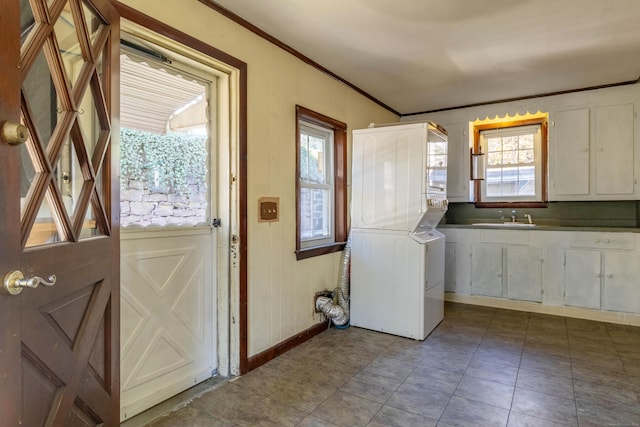 washroom featuring tile patterned flooring, crown molding, stacked washing maching and dryer, and sink