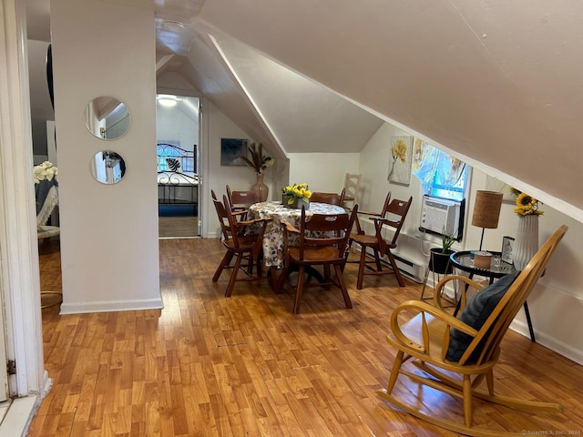 dining space featuring light hardwood / wood-style floors, vaulted ceiling, cooling unit, and a baseboard radiator