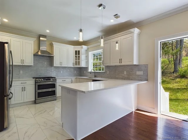 kitchen featuring pendant lighting, white cabinets, wall chimney exhaust hood, decorative backsplash, and stainless steel appliances