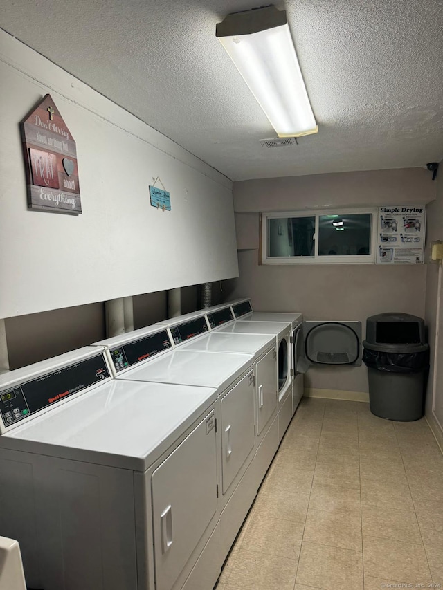 washroom with washing machine and dryer, light tile patterned floors, and a textured ceiling