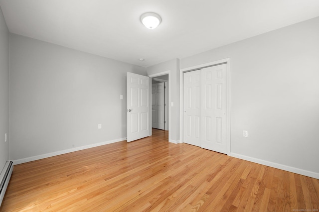 unfurnished bedroom featuring light hardwood / wood-style floors, a baseboard radiator, and a closet