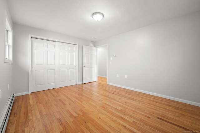 unfurnished bedroom with a closet, light hardwood / wood-style floors, and baseboard heating