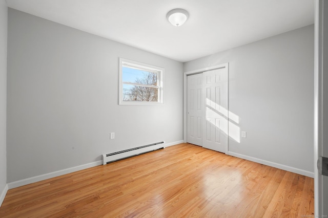 unfurnished room with light wood-type flooring and a baseboard heating unit