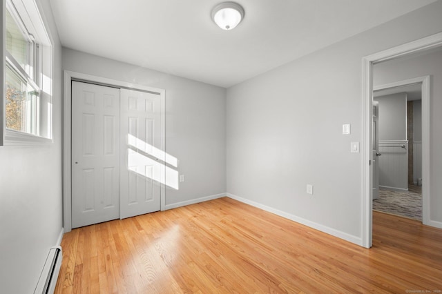 unfurnished bedroom featuring a closet, hardwood / wood-style flooring, and baseboard heating