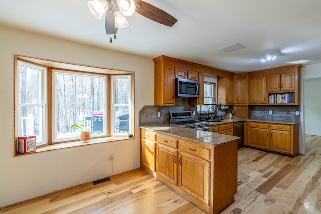 kitchen featuring appliances with stainless steel finishes, backsplash, dark stone counters, sink, and light hardwood / wood-style floors