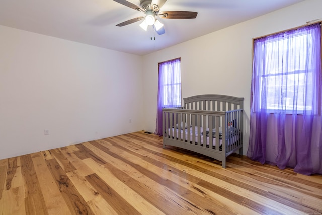 bedroom featuring light wood-type flooring, a nursery area, and ceiling fan