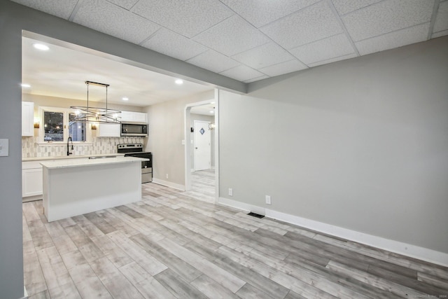 kitchen featuring light wood-type flooring, stainless steel appliances, white cabinets, a center island, and hanging light fixtures