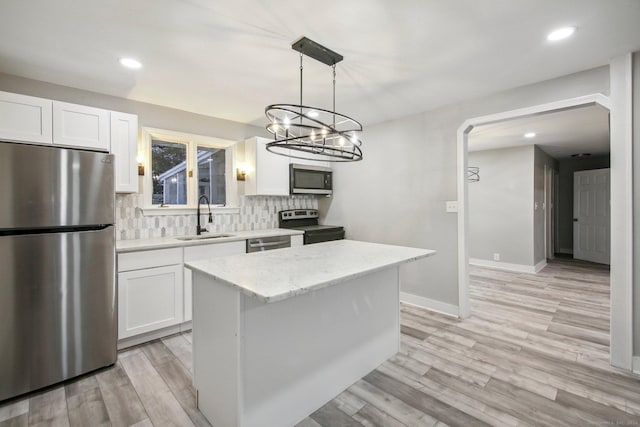 kitchen with white cabinetry, sink, decorative light fixtures, a kitchen island, and appliances with stainless steel finishes