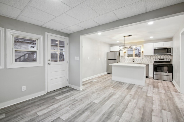 kitchen featuring decorative light fixtures, stainless steel appliances, white cabinetry, and light hardwood / wood-style flooring