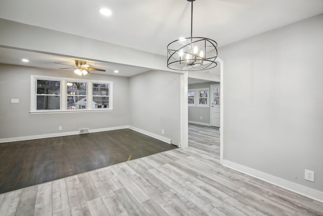 unfurnished dining area featuring ceiling fan with notable chandelier and wood-type flooring