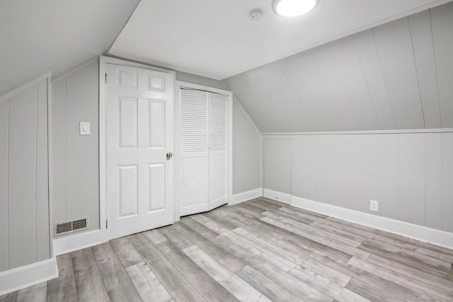 bonus room with lofted ceiling, wood walls, and light wood-type flooring