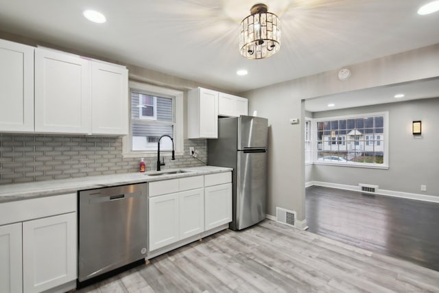 kitchen with stainless steel appliances, sink, light hardwood / wood-style floors, white cabinetry, and hanging light fixtures